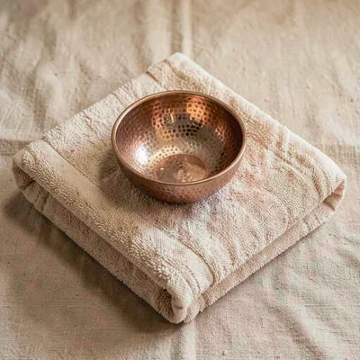 Warm flat lay of a folded hammam towel with a hammered copper bowl resting on to