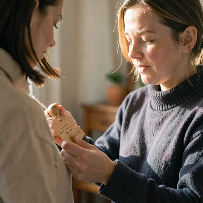Side-light portrait of a parent reading a paper tag tied to a wooden rattle, gen