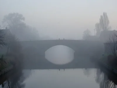 A stone bridge arching over a canal, the far end dissolving into thick fog, fain