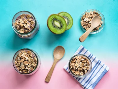 Knolled smoothie-bowl ingredients halved kiwi a glass jar of granola a wooden sp