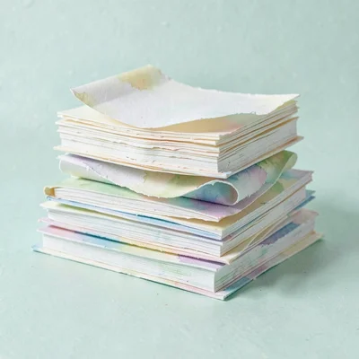 Papercraft pile of stacked cut-paper books with curling pages, calm mint backdro