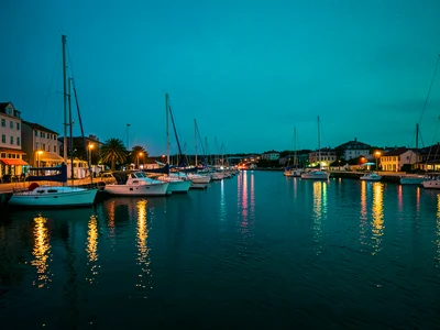 A harbor at blue hour, warm lights from boats and shore buildings, the water and