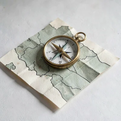 Layered papercraft tableau of a paper compass spinning over a folded map, dusty 