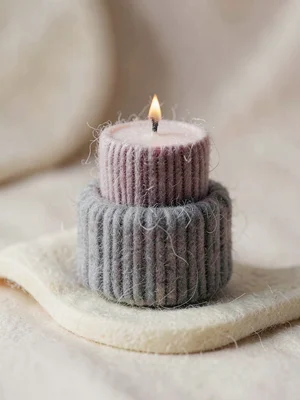Lit-tipped soft-plum knit candle in a heather-grey ribbed holder with a tiny moh
