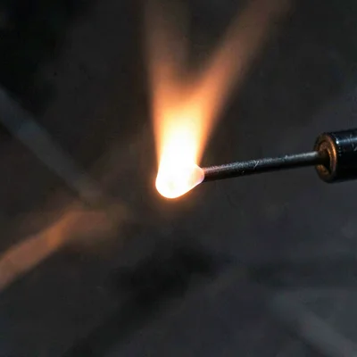 Mineral-cut macro of molten glass glowing white-orange at the end of a blow pipe