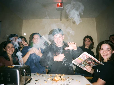 Smoke billowing from a toaster, person fanning frantically with a magazine, burn