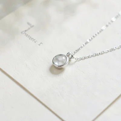 Clean still of a single pendant on a silver chain on cream paper