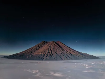 Volcanic peak rising above inversion layer into clear dark upper atmosphere