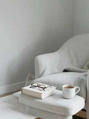 Stack of books with reading glasses on top, cup of tea, cozy armchair corner