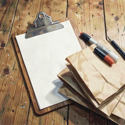 Warm flat-lay of a clipboard, marker, and stack of paper bags on a worn wooden s