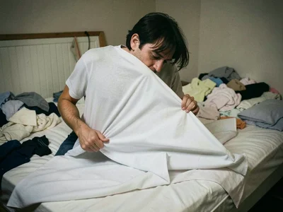 A person wrestling with a fitted sheet, the elastic corners pulling free as they