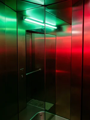 Mirror reflection in elevator, metallic surfaces catching green and red neon