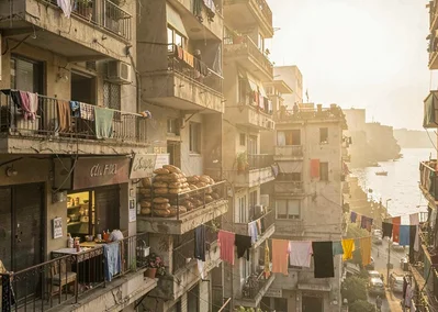 Dusty golden Cairo haze compressing apartment layers, bakery storefront with sta