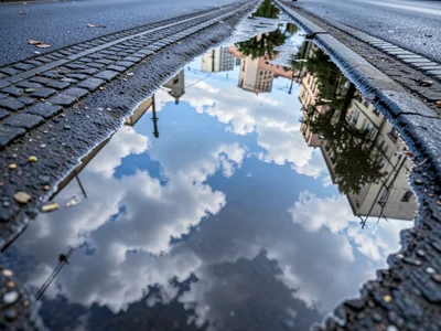 Chain of puddles in tire tracks reflecting moving clouds, elongated mirrors in p