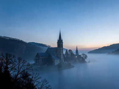Church spire rising above fog sea catching first light