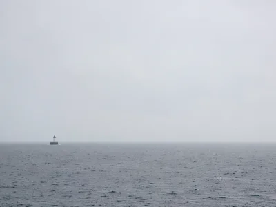 Minimal lighthouse small at edge of frame with vast grey ocean and sky