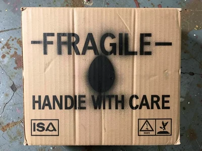 Spray-stenciled "FRAGILE — HANDLE WITH CARE" on a corrugated cardboard box with 