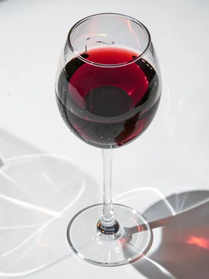 Wine glass with red wine, light refracting through liquid, caustics dancing on w