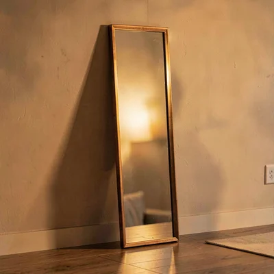 Vertical warm still-life of a tall hand mirror leaning against a wall, reflectin