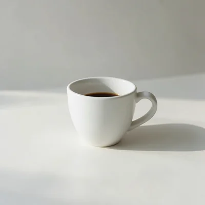 Minimalist photography of a single white coffee cup on a clean matte off-white surface, soft natural window light from t