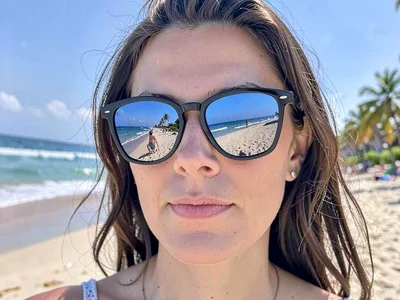 A woman's mirrored sunglasses reflecting beach scene she's watching, eyes hidden