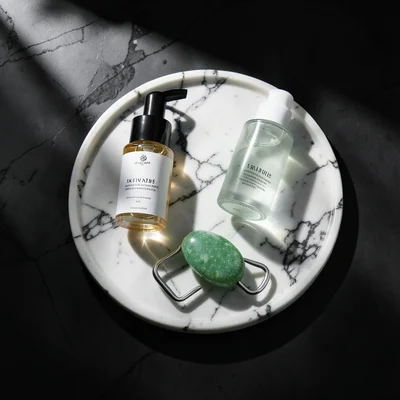 Skincare routine flat lay: cleanser, serum, moisturizer, jade roller on marble t