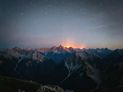 Alpenglow on distant peaks while upper sky shows faint stars