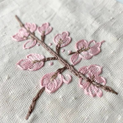 Close-up of hand-stitched cherry blossom branch on cotton, pink silk thread