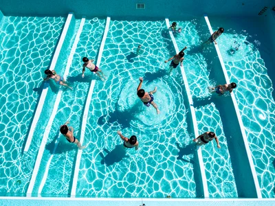 Children playing in a wave pool from above, the wave pattern creating parallel w