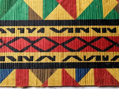 Kente strip detail flat-lay — warp and weft texture visible, top-down macro