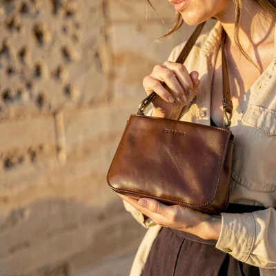 Warm vertical campaign of a small flap bag held loosely in a model's hand, golde
