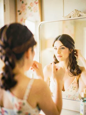 Woman braiding her hair in front of a vanity mirror, only her reflection in focu