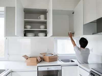 A kitchen being unpacked in a new apartment, upper cabinets with doors open — on
