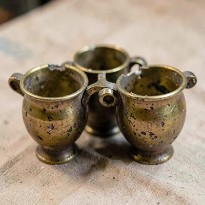 Worn-material study of a battered brass cups-and-balls set, lips dented with use