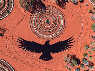 Desert hawk shadow on red sand below — spread wings as dark silhouette, top-down