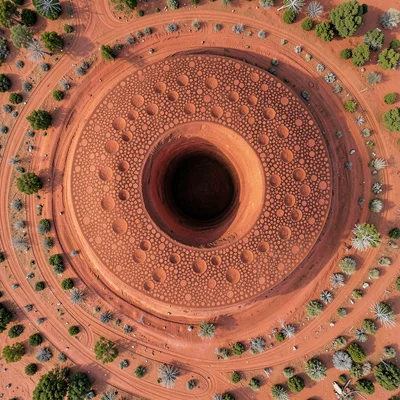 Circular termite mound from above, tunnel openings as concentric rings in red ea
