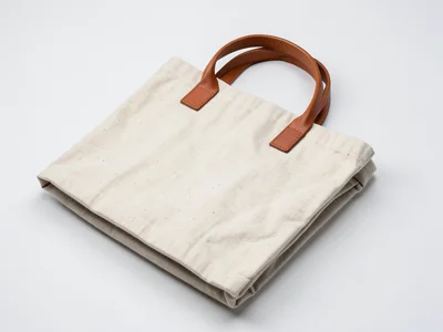 A linen tote bag, natural color with leather handles, folded flat to show constr