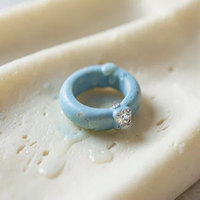 Wedded faded-blue ring shape with a slumped band and thumb-pressed gem setting, 