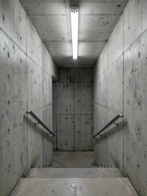 A council housing estate stairwell — board-formed concrete walls, fluorescent li