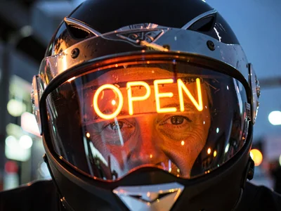 Motorcycle helmet visor reflecting a neon sign that reads OPEN, the rider's eyes