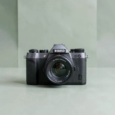 Catalog square of a camera with prime lens against a sage green color block, bal