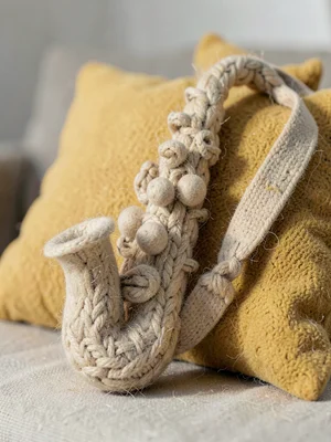 Saxophone in chunky knit with bobbled keys and a felted strap leaning against a 