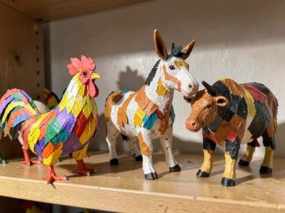 A collection of small papier-mâché animals on a shelf — roosters, donkeys, and b
