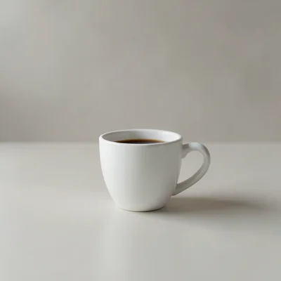 Minimalist photography of a single white coffee cup centered on a clean matte surface, soft natural window light, subtle