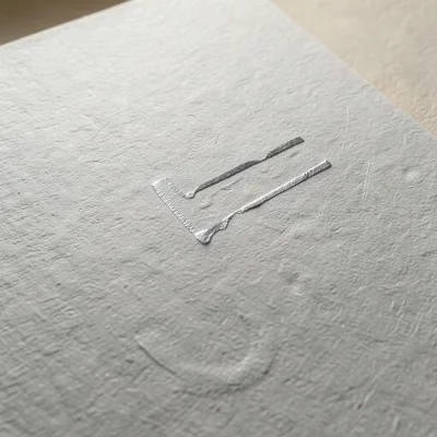 Silver foil on uncoated paper, metallic stamp absorbing slightly into paper fibe