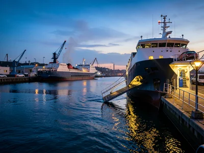 A car ferry's bow door opening as it approaches a dock, the ramp descending, veh