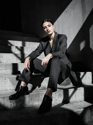 Model sitting on concrete steps in monochrome outfit, architectural shadows, edi