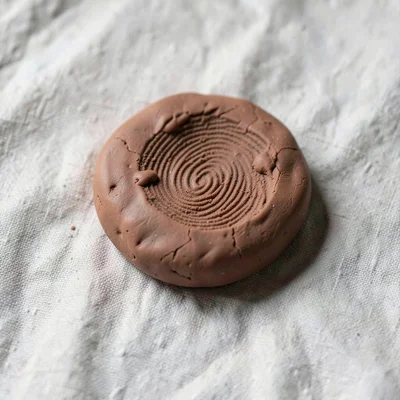 Aged terracotta clay marble with thumbprint dimples around its surface, on plain
