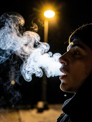 Person exhaling visible breath in cold air, backlit by golden streetlight, winte
