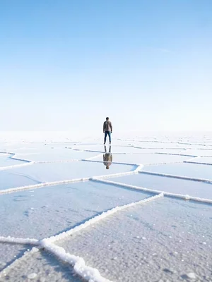 Single person standing on flooded salt flat — tiny figure with their perfect ref